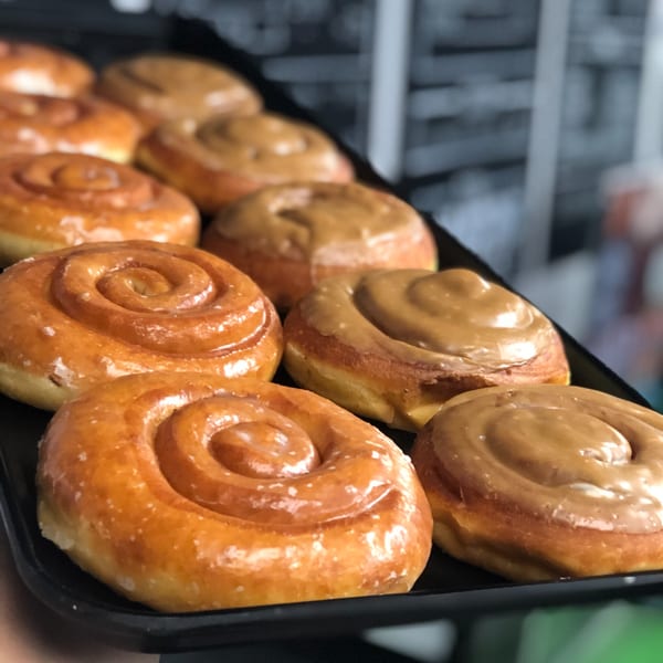 A tray of Donut Factory cinnamon roll donuts, some with glaze and some with caramel frosting.