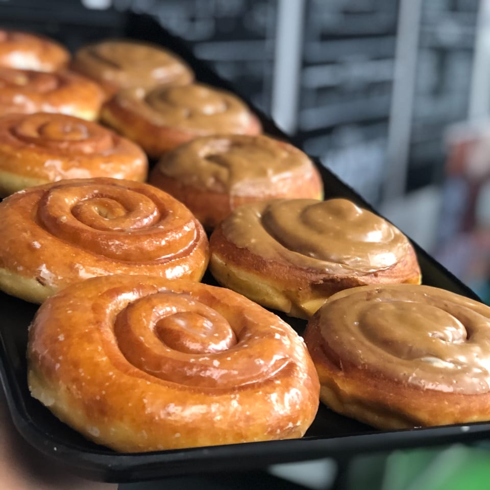 A tray of Donut Factory cinnamon roll donuts, some with glaze and some with caramel frosting.