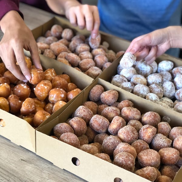 Hands reaching into boxes of glazed, cinnamon sugar, and powdered sugar donut holes from Donut Factory.