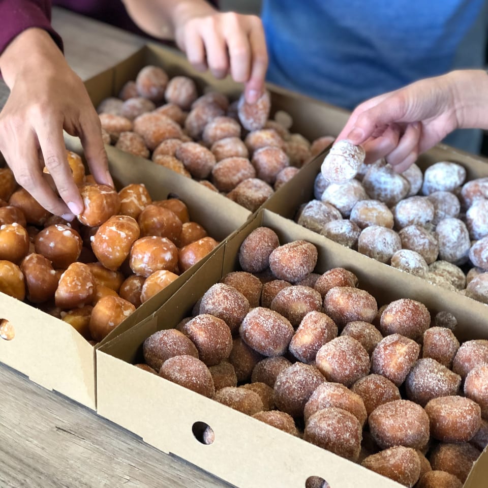 Hands reaching into boxes of glazed, cinnamon sugar, and powdered sugar donut holes from Donut Factory.