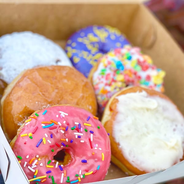 A box of assorted Donut Factory donuts, including pink with sprinkles, glazed, powdered, and cereal-topped.