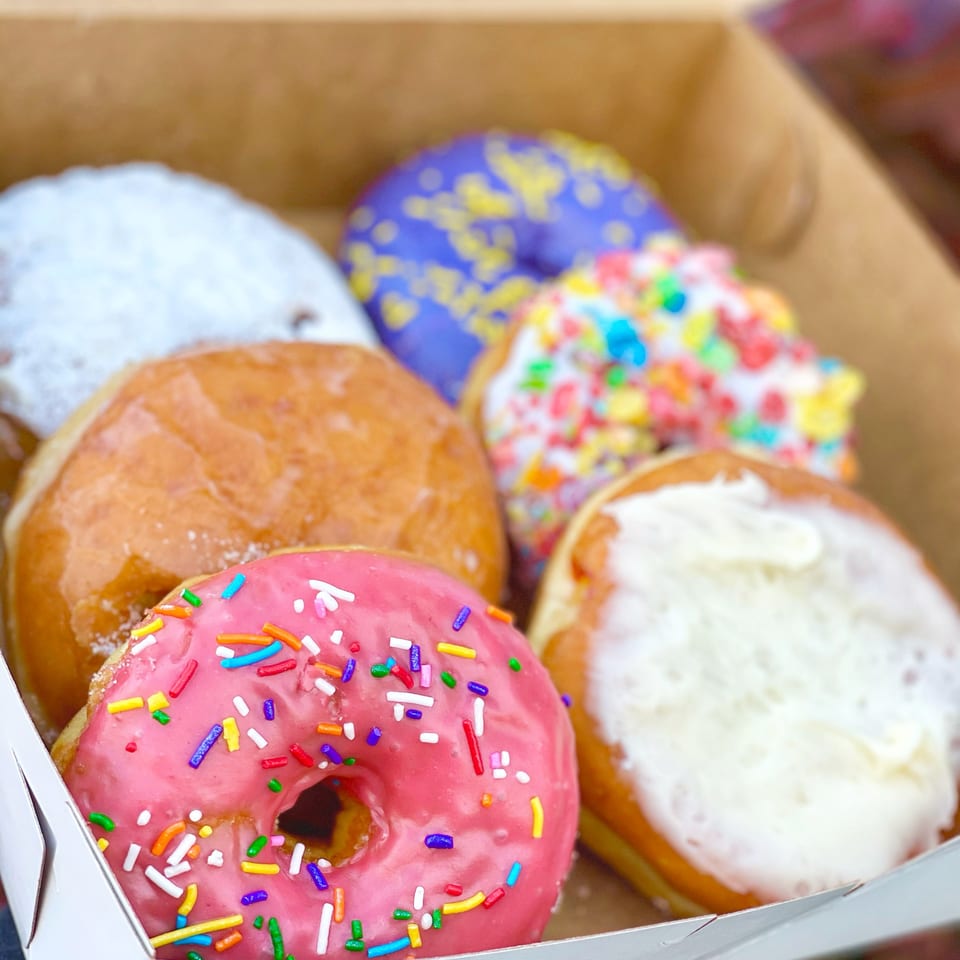 A box of assorted Donut Factory donuts, including pink with sprinkles, glazed, powdered, and cereal-topped.