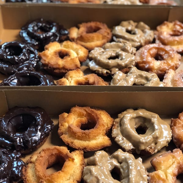 Two rows of assorted Donut Factory donuts, including chocolate, plain, and glazed, in a box.