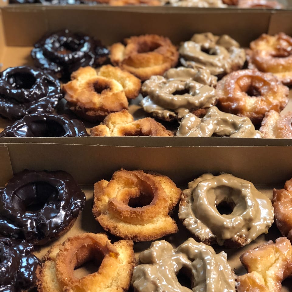 Two rows of assorted Donut Factory donuts, including chocolate, plain, and glazed, in a box.