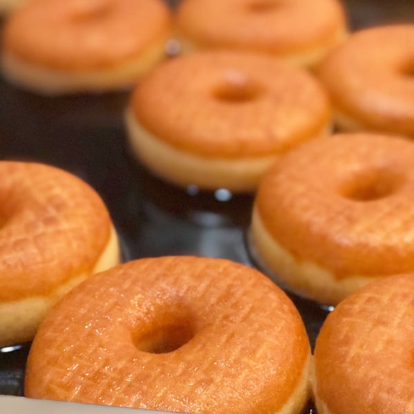 Close-up of multiple freshly glazed donuts from Donut Factory on a dark surface.