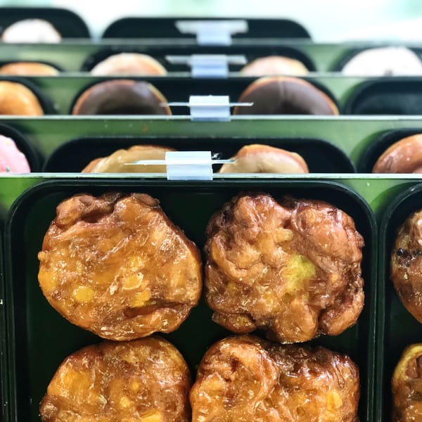 Rows of glazed apple fritters and various donuts in display cases at Donut Factory.