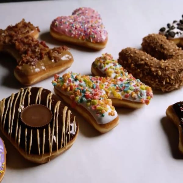 Assortment of Donut Factory donuts, including bacon, heart-shaped, cereal-topped, and Reese's varieties.