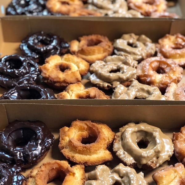 Three rows of assorted Donut Factory donuts, including chocolate, plain, and glazed varieties, in a box.
