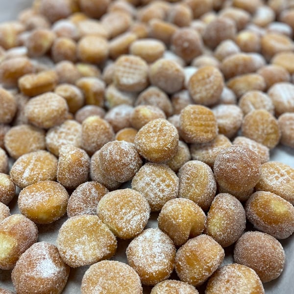 Close-up of numerous golden-brown donut holes, generously coated in white powdered sugar.