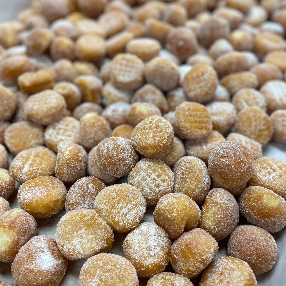 Close-up of numerous golden-brown donut holes, generously coated in white powdered sugar.