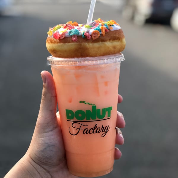 Hand holding a Donut Factory drink with a Froot Loops donut on top.