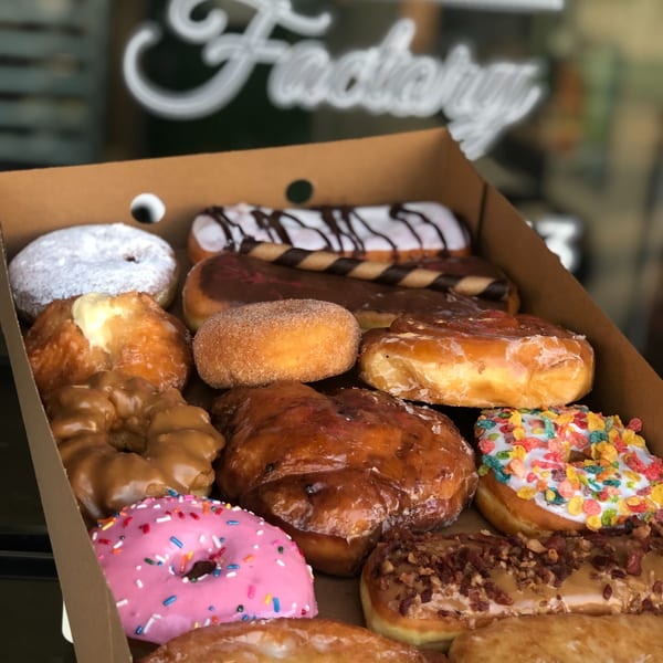 A box of assorted Donut Factory donuts, including glazed, powdered, frosted, and sprinkled varieties.