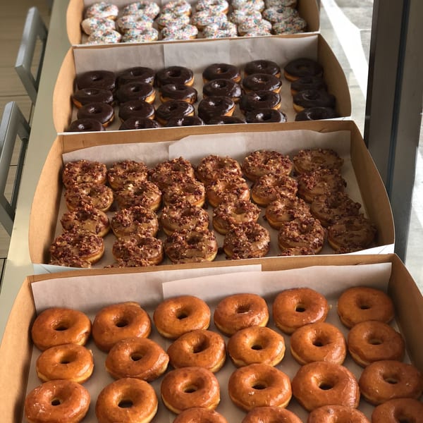 Four boxes of Donut Factory donuts, including glazed, chocolate, and nut-topped varieties.